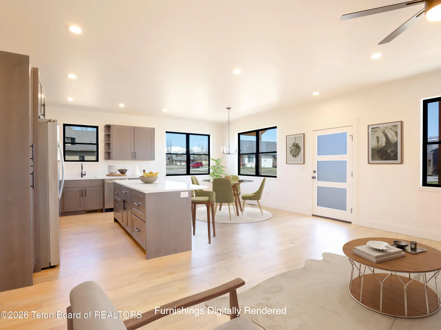 Open-concept kitchen and dining area with light wood floors, gray cabinets, and a white island. A round table with green chairs sits near large windows.