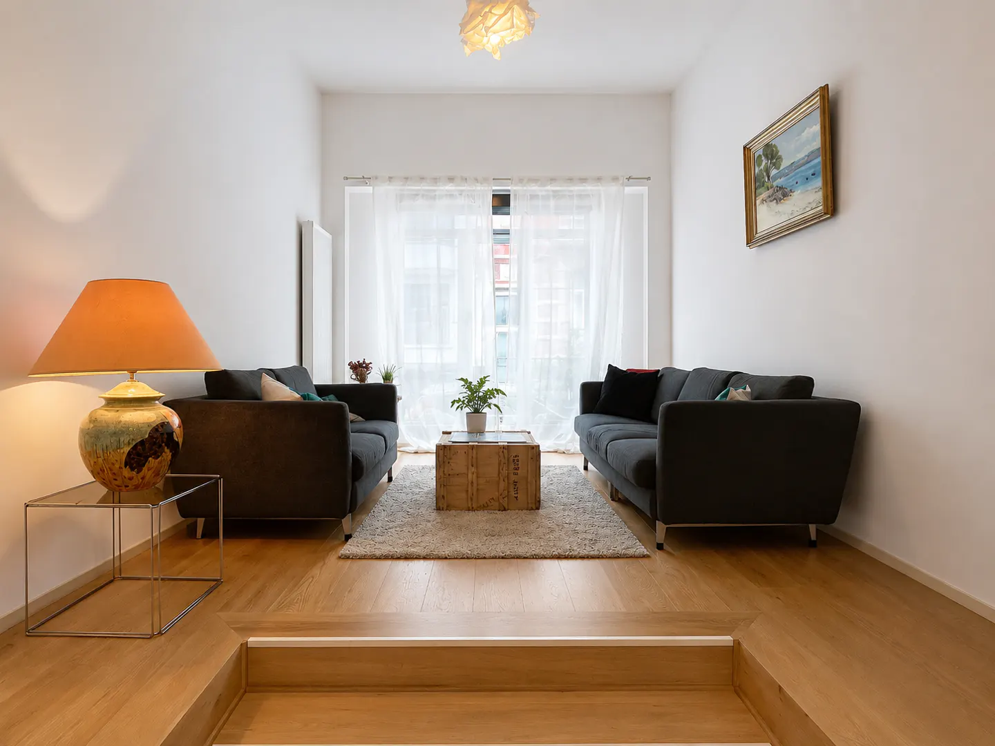 Living room with two gray sofas facing each other, a wooden crate coffee table, and a lamp with an orange shade.