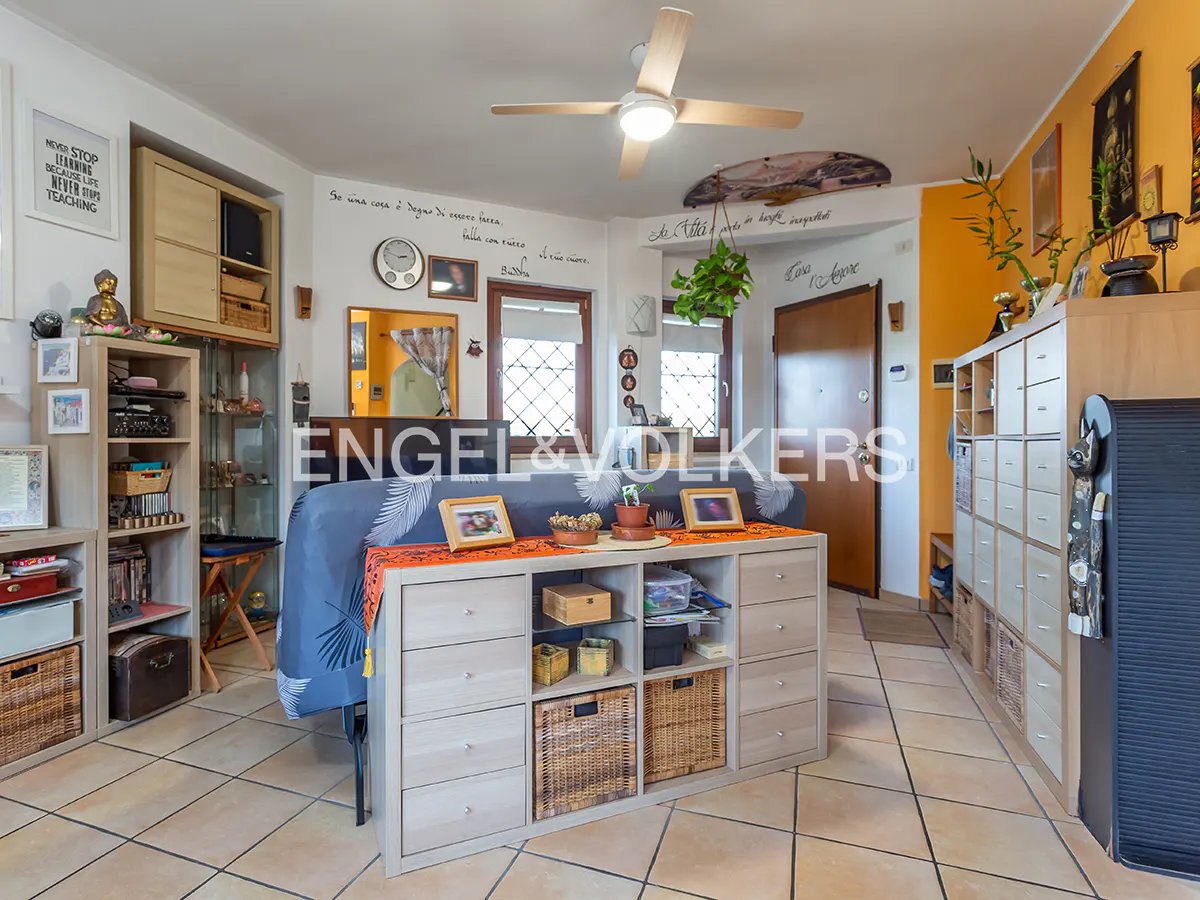 A bright living room with beige tile floors, a ceiling fan, and built-in storage. The walls are white and yellow.