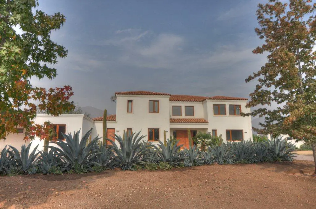 A two-story white house with a red tile roof, brown trim, and agave plants in front.