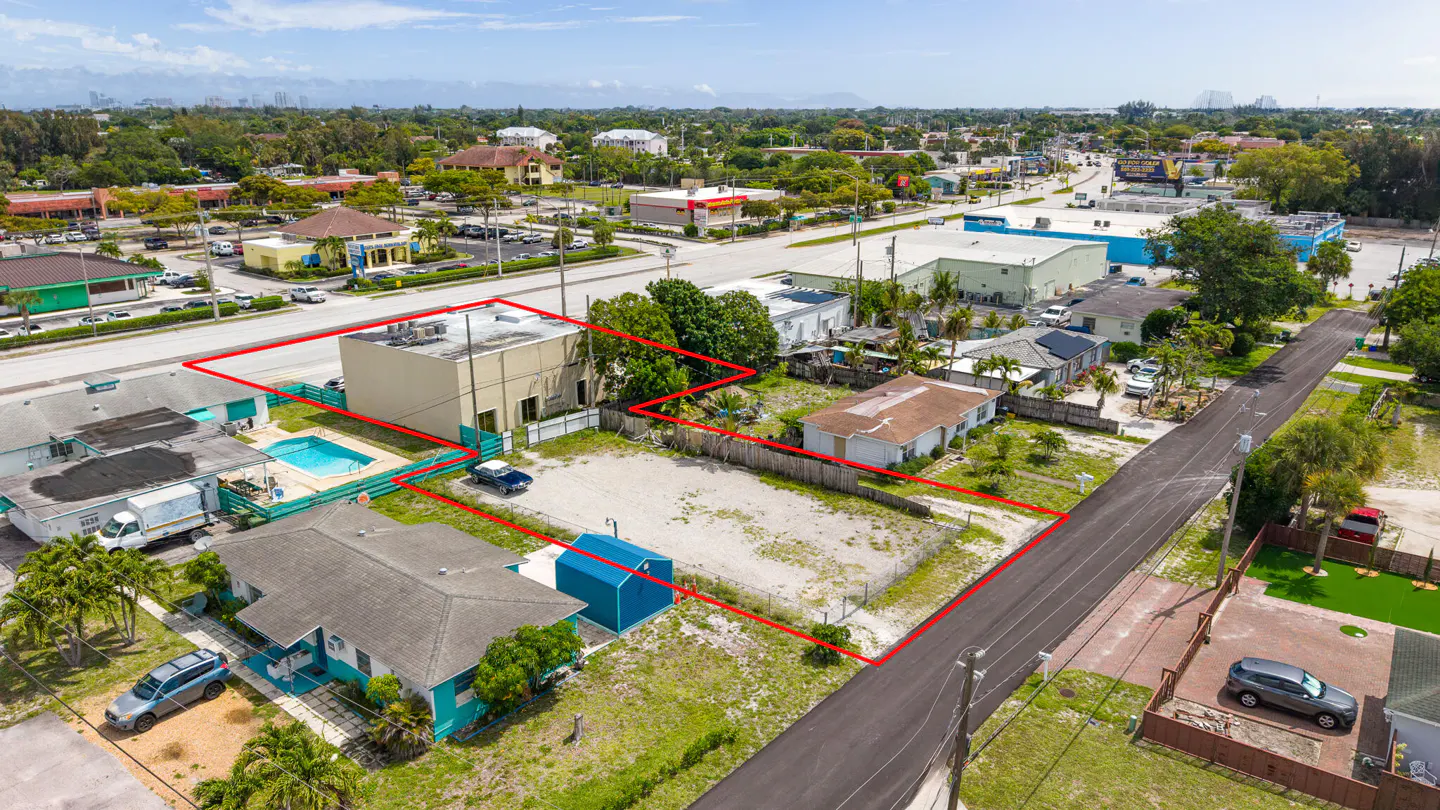 Aerial view of a property outlined in red, featuring a building, pool, and vacant lot in a suburban neighborhood.
