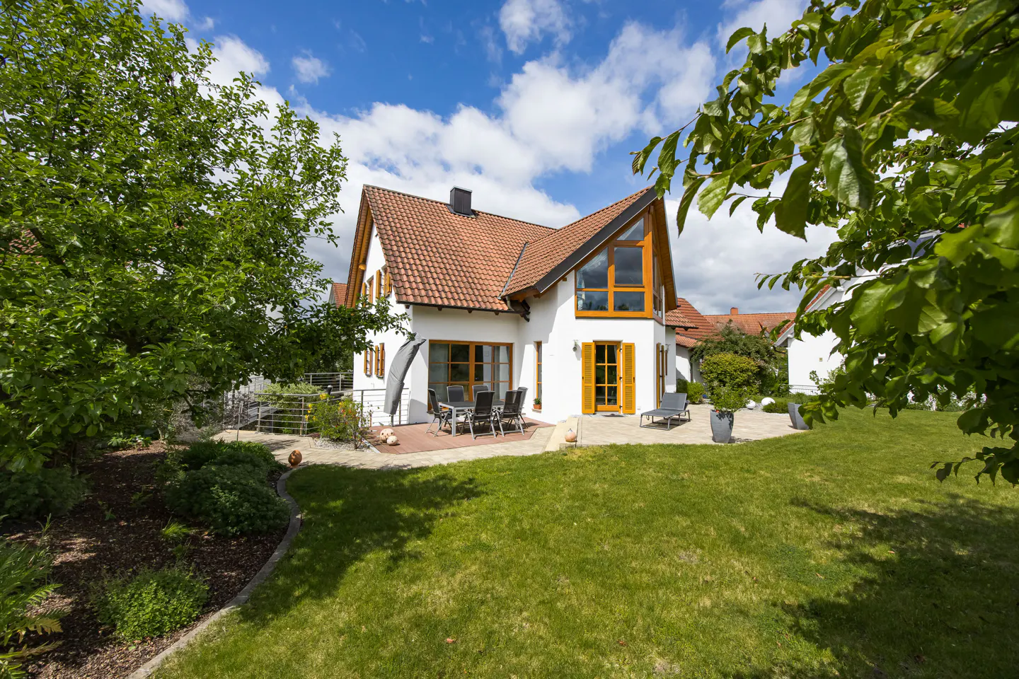 A white house with a red tile roof, yellow trim, and a green lawn under a blue sky with white clouds.