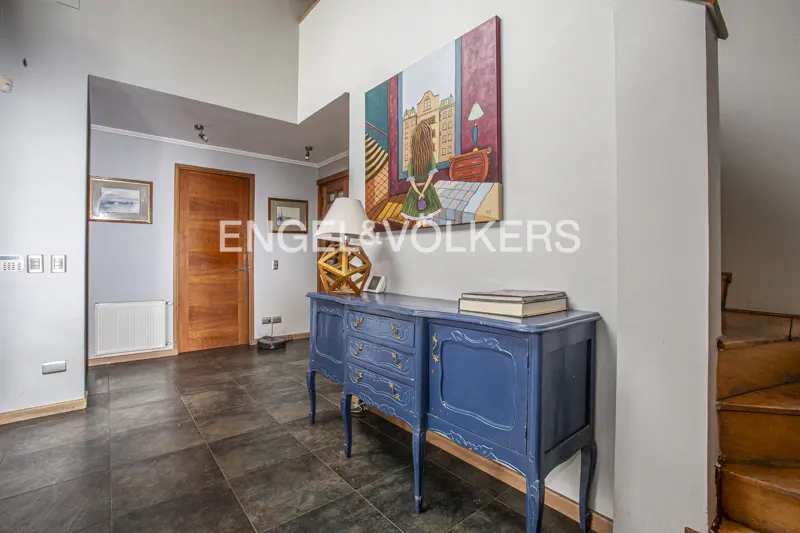 Foyer with blue console table, lamp, and painting. Wood door and dark tile floor. Engel & Volkers logo visible.