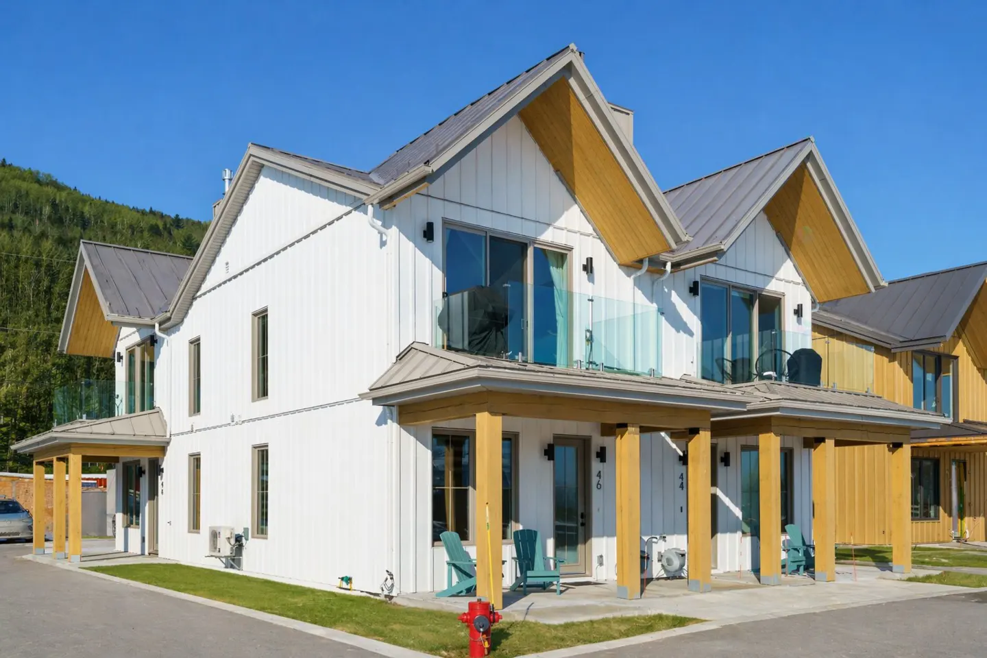 Exterior view of modern white townhouses with gray roofs and wood accents, set against a backdrop of green trees and a clear blue sky.