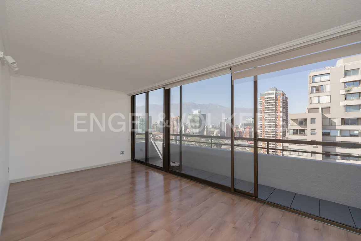 Bright, empty room with wood floors and white walls. Large sliding glass doors open to a balcony with a city view.