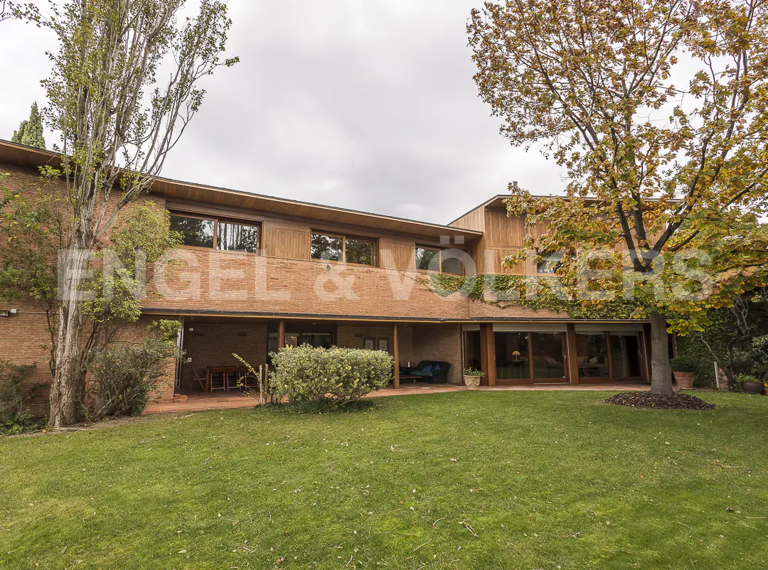 Two-story brick house with a green lawn and trees. The house has a flat roof and large windows.