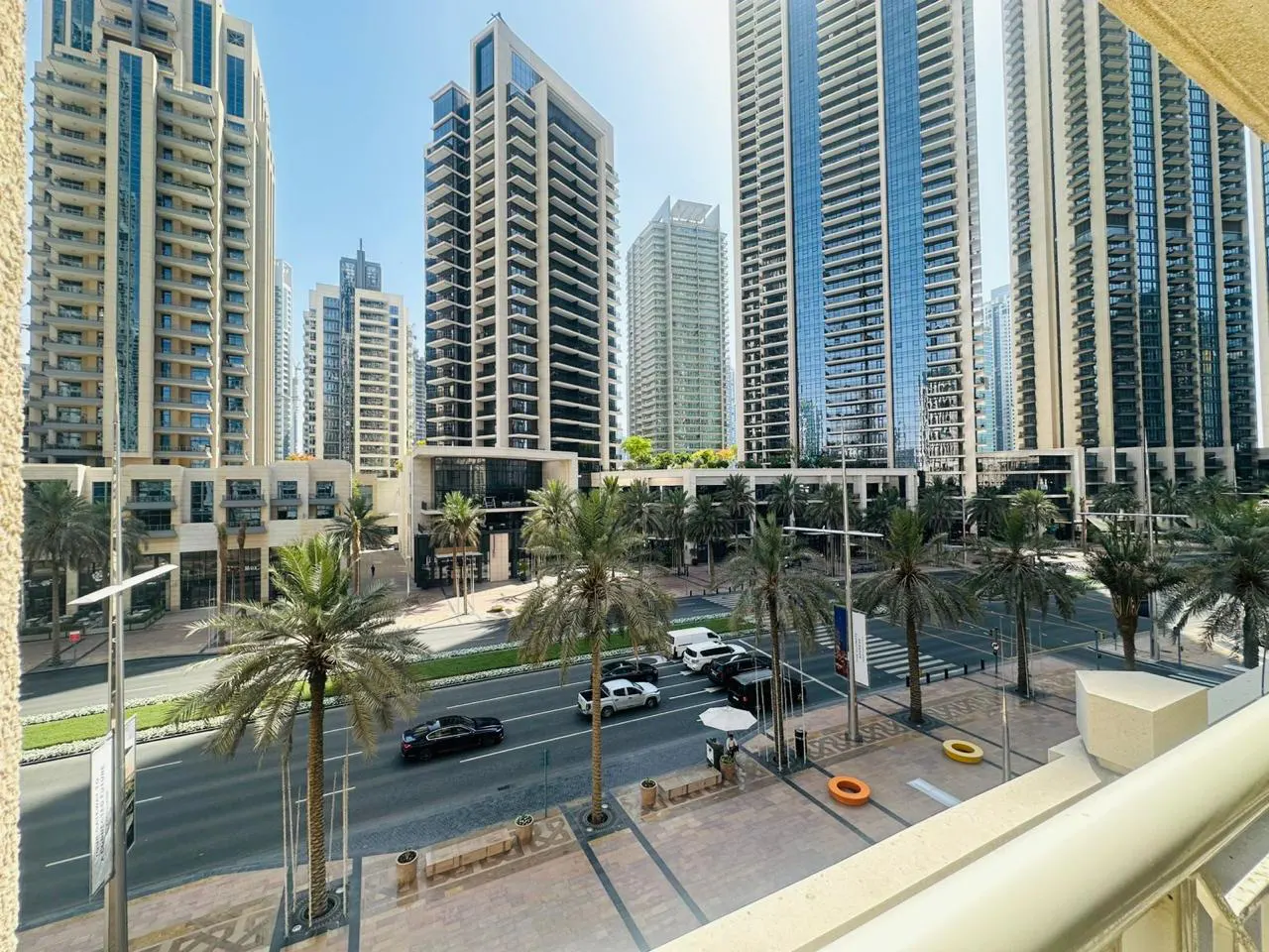 View from a balcony overlooking a city street lined with palm trees and tall buildings on a sunny day.