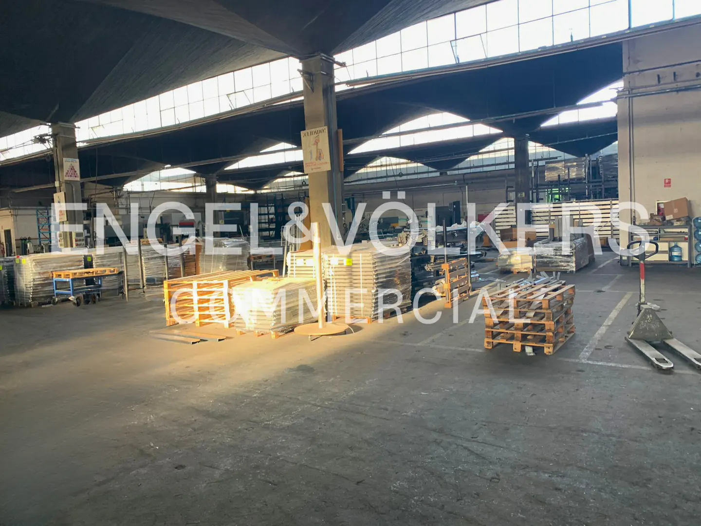 Spacious industrial warehouse with concrete floors, high vaulted ceilings, and wooden pallets stacked with materials.