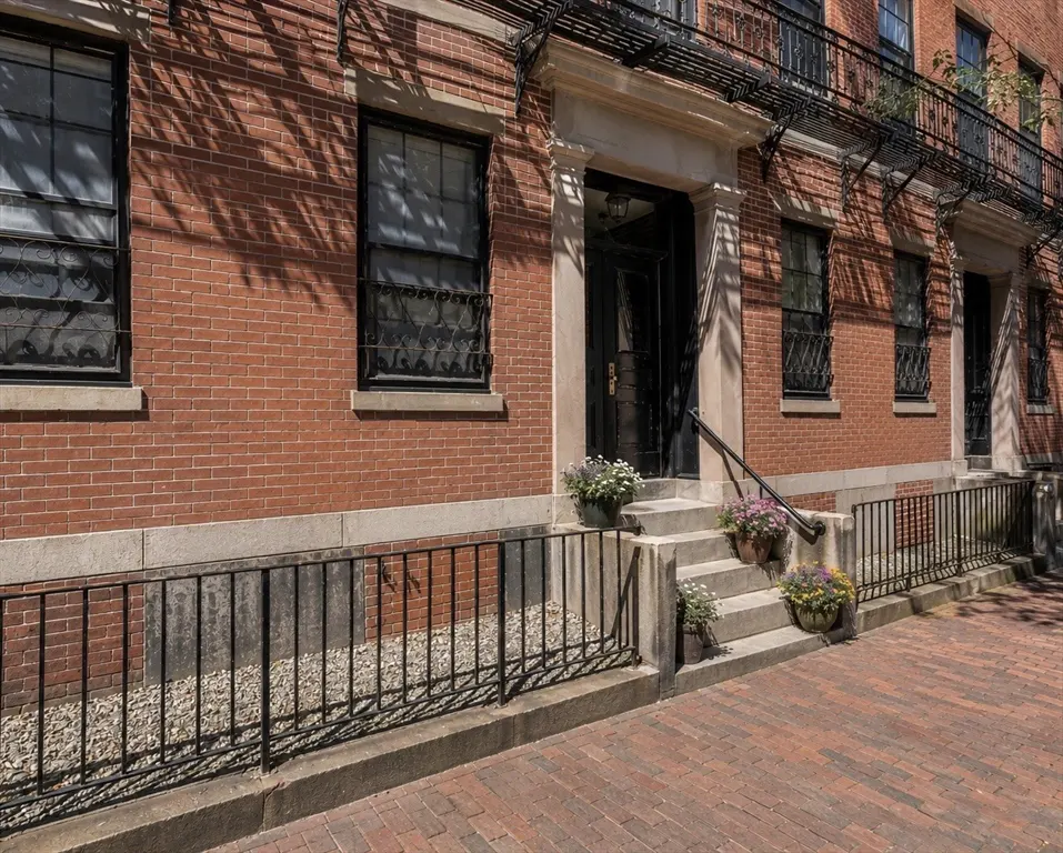 Red brick apartment building exterior with black iron railings, stone steps, and potted flowers at the entrance.