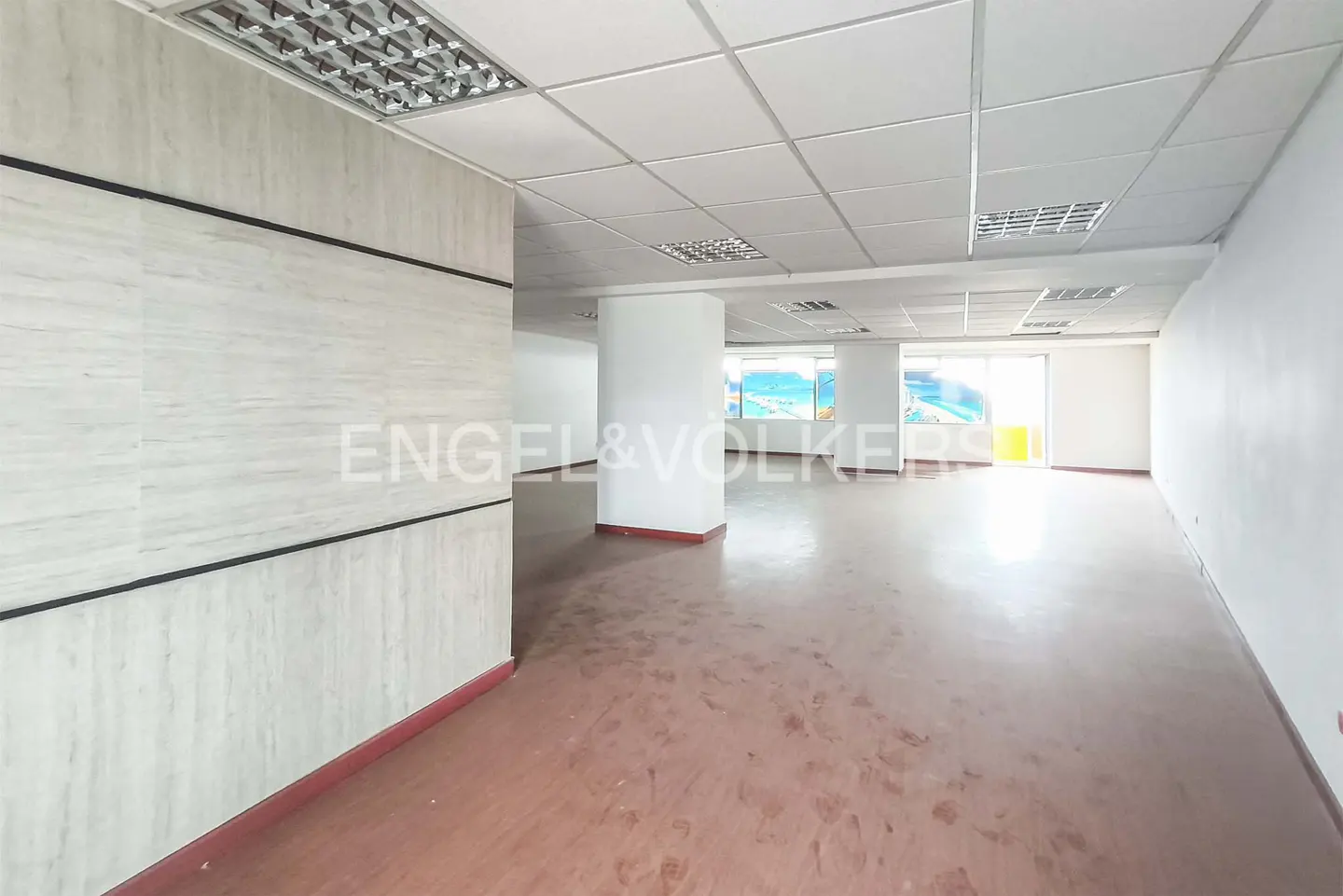 An empty office space with white walls, a red floor, and a white ceiling with fluorescent lights.