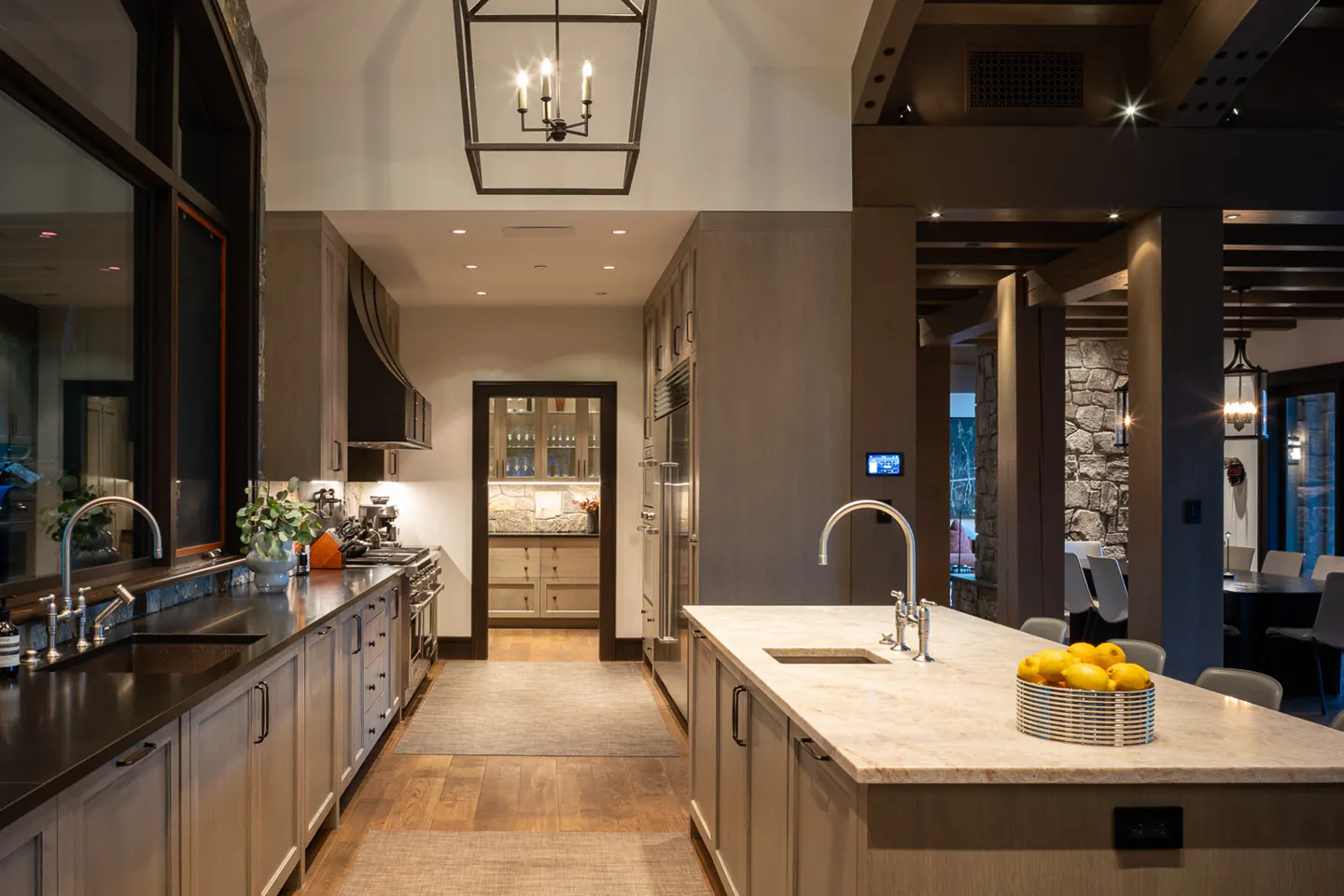 A modern kitchen with light wood floors, gray cabinets, and a large island with a bowl of lemons.