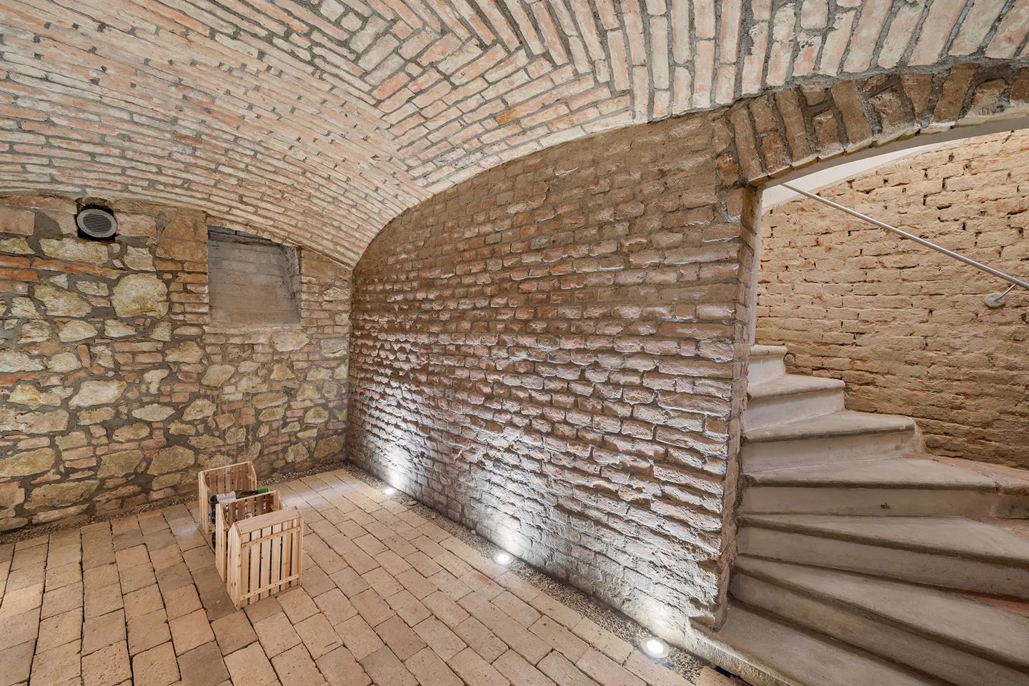 Arched brick cellar with stone walls, brick floor, and stairs. Two wooden crates sit on the floor.