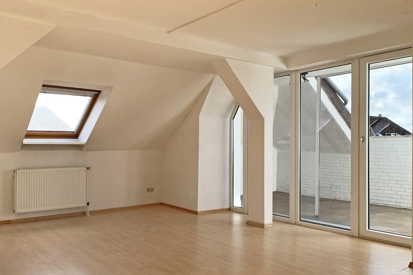 Empty attic room with light wood floors, white walls, a radiator, a skylight, and glass doors leading to a balcony.