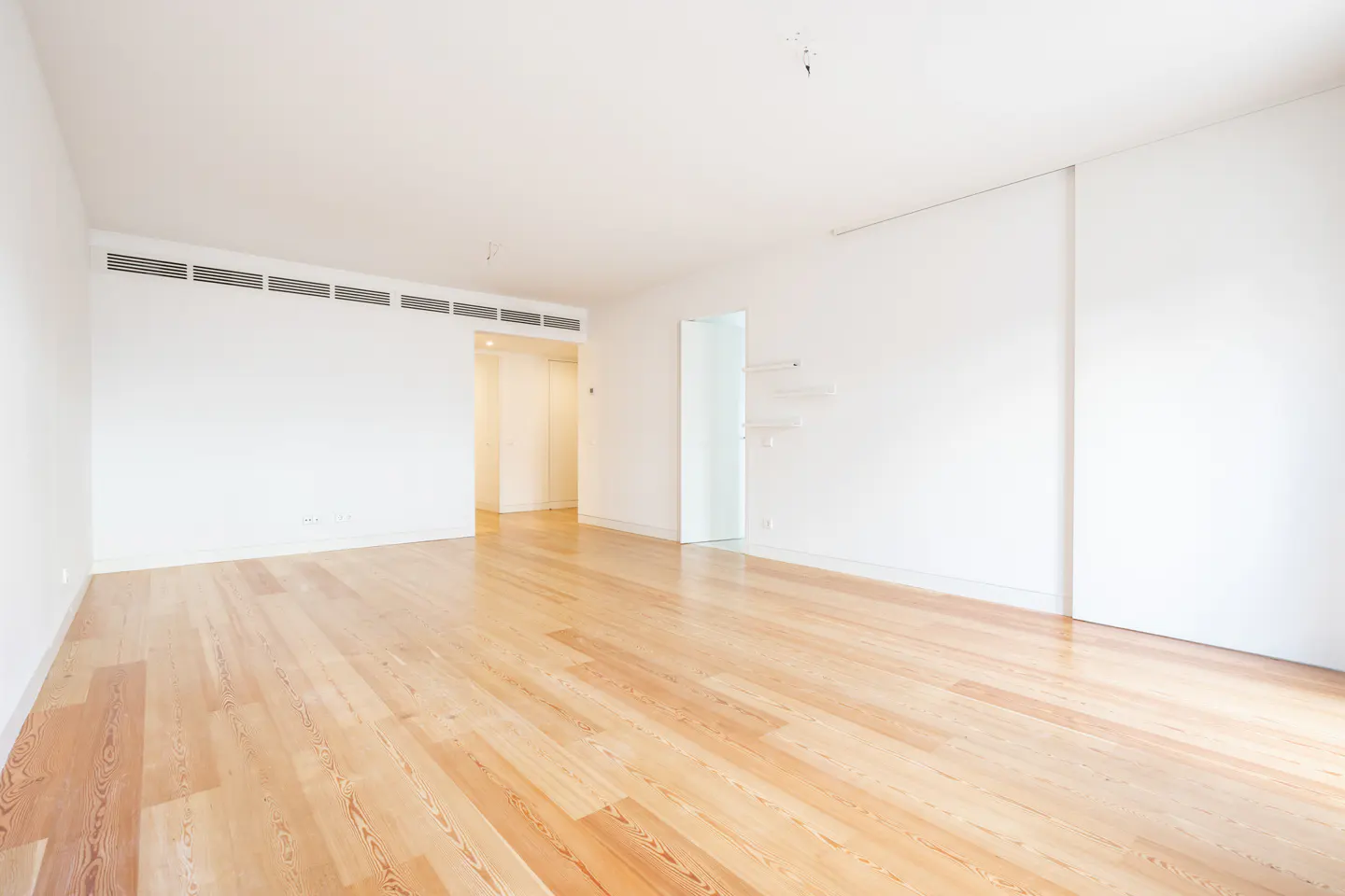 Empty room with light wood floors and white walls. A doorway is visible in the background.