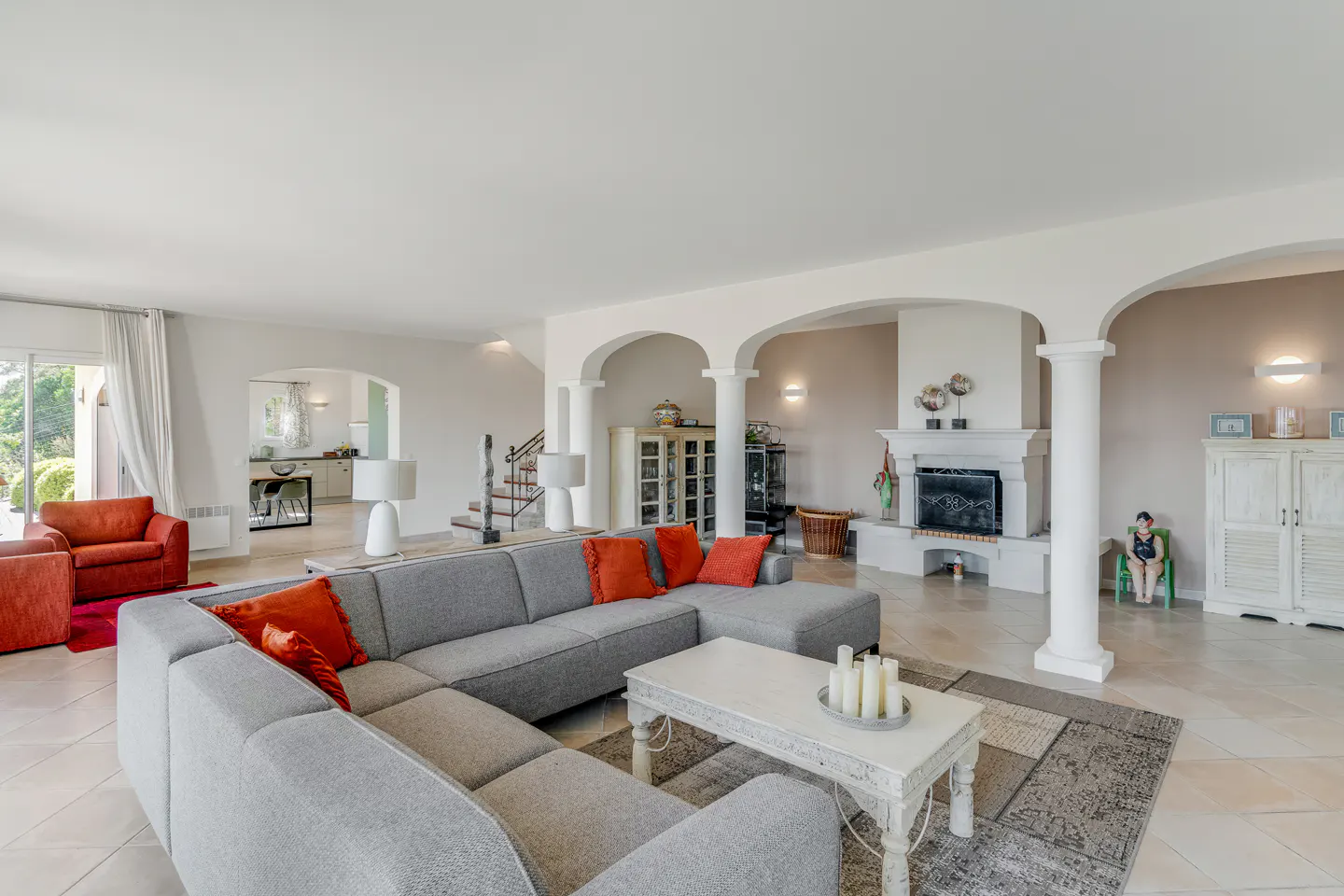 Spacious living room with gray sectional sofa, orange pillows, white coffee table with candles, and arched doorways.