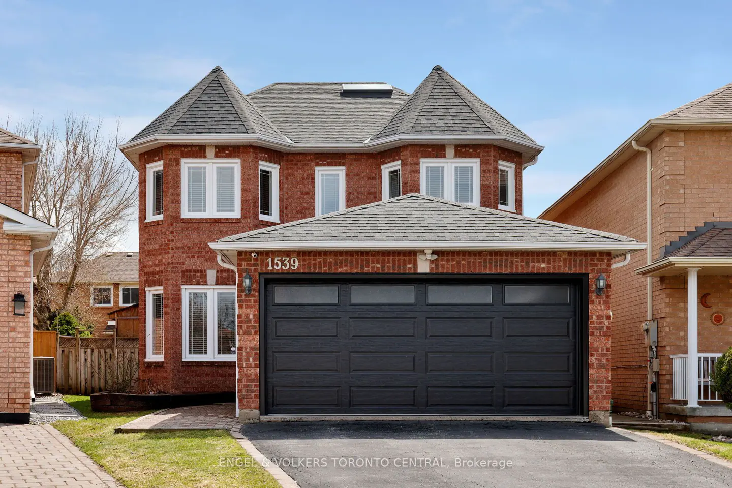 Two-story red brick house with a gray roof and a black garage door. The house number 1539 is visible above the garage.