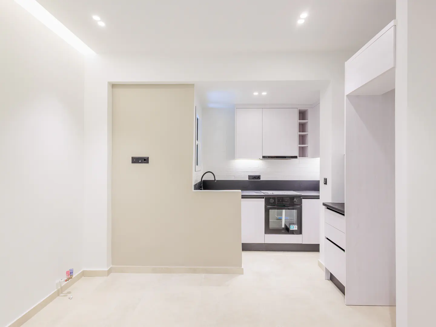 Bright, modern kitchen with white cabinets, black countertops, and stainless steel appliances. The walls are white and beige.