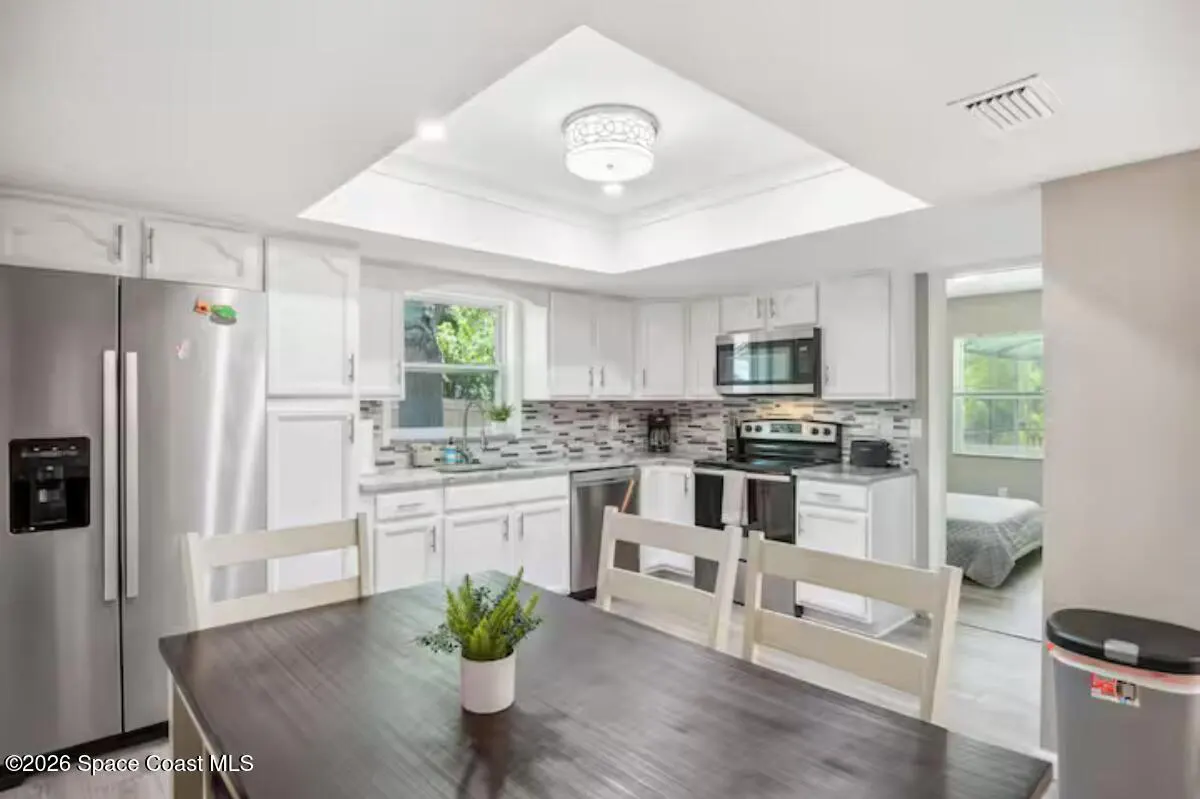 A bright kitchen with white cabinets, stainless steel appliances, and a dark wood table with white chairs.