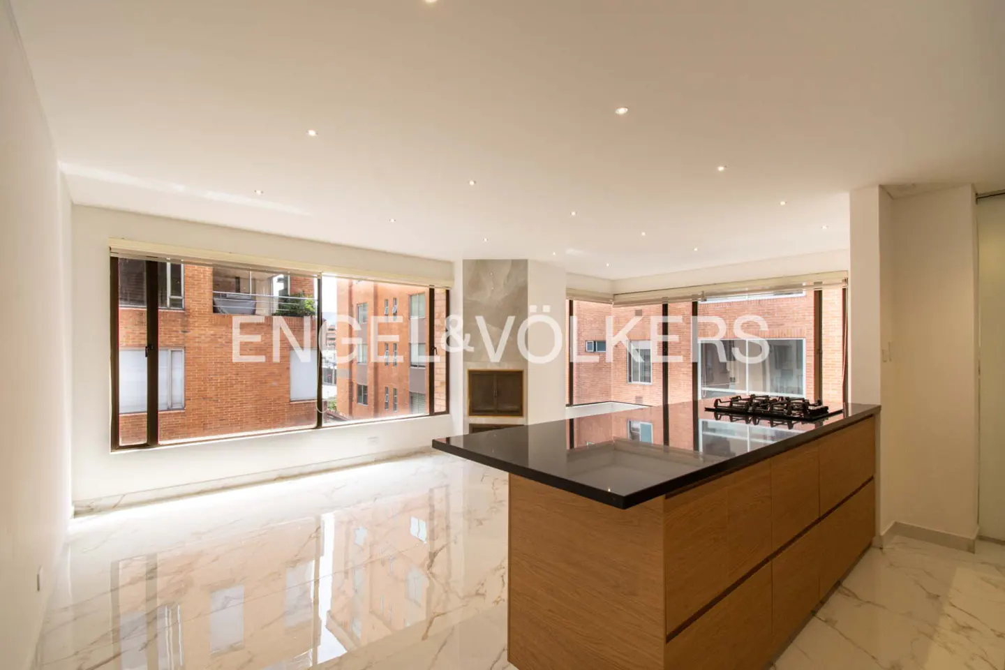 Bright, modern apartment with marble floors, a kitchen island with a black countertop, and large windows overlooking a brick building.
