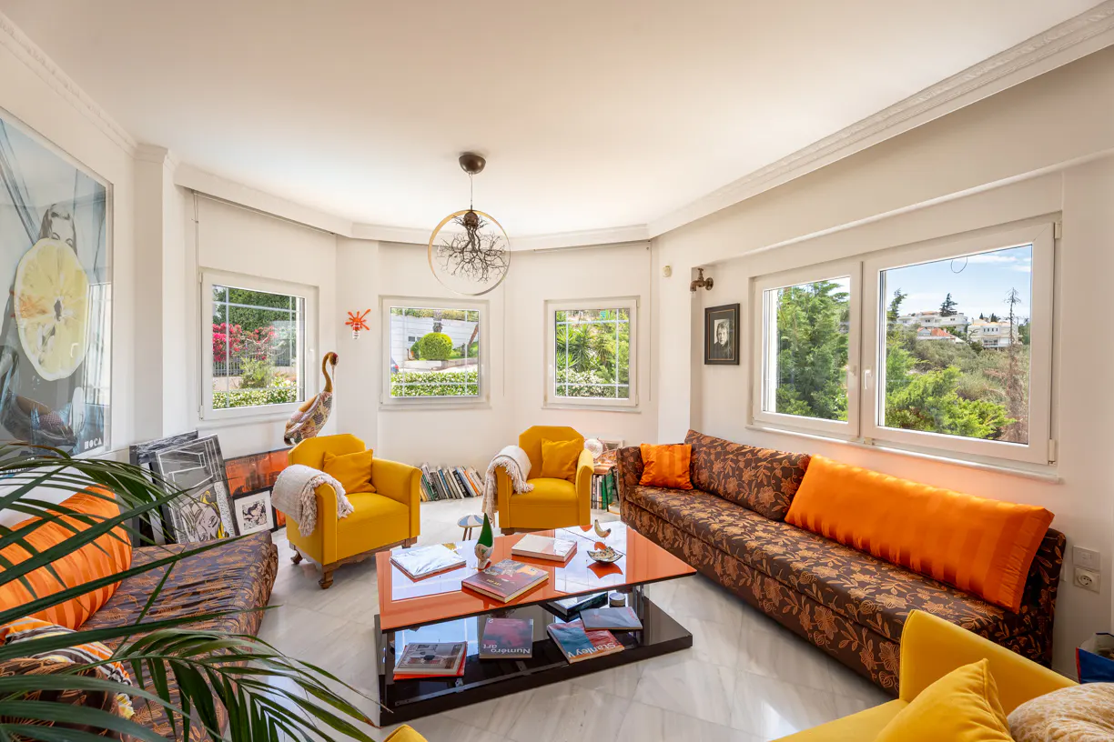 Bright living room with two yellow armchairs, a floral sofa with orange cushions, and a modern orange coffee table.