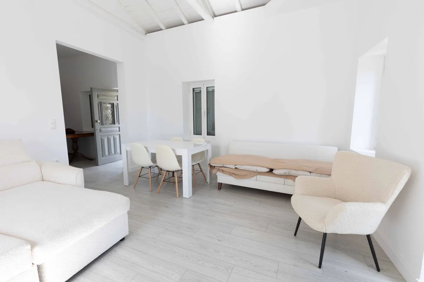 Bright, all-white living room with a sofa, chair, table, and chairs. A doorway leads to another room.