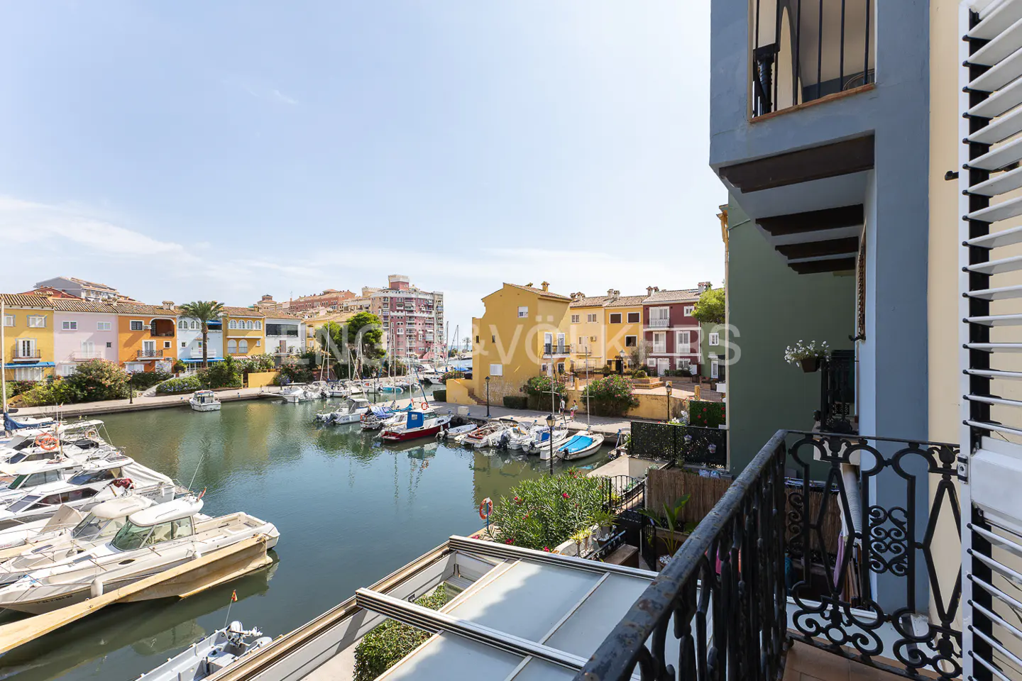 View from a balcony overlooking a marina filled with boats, with colorful buildings in the background under a blue sky.