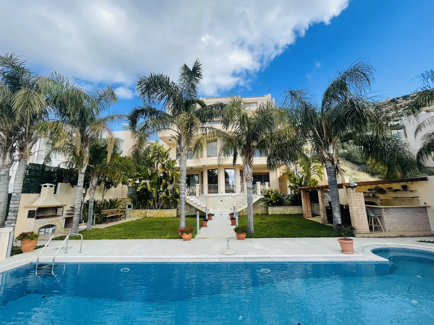Luxury home exterior with a blue pool, palm trees, and a clear sky.
