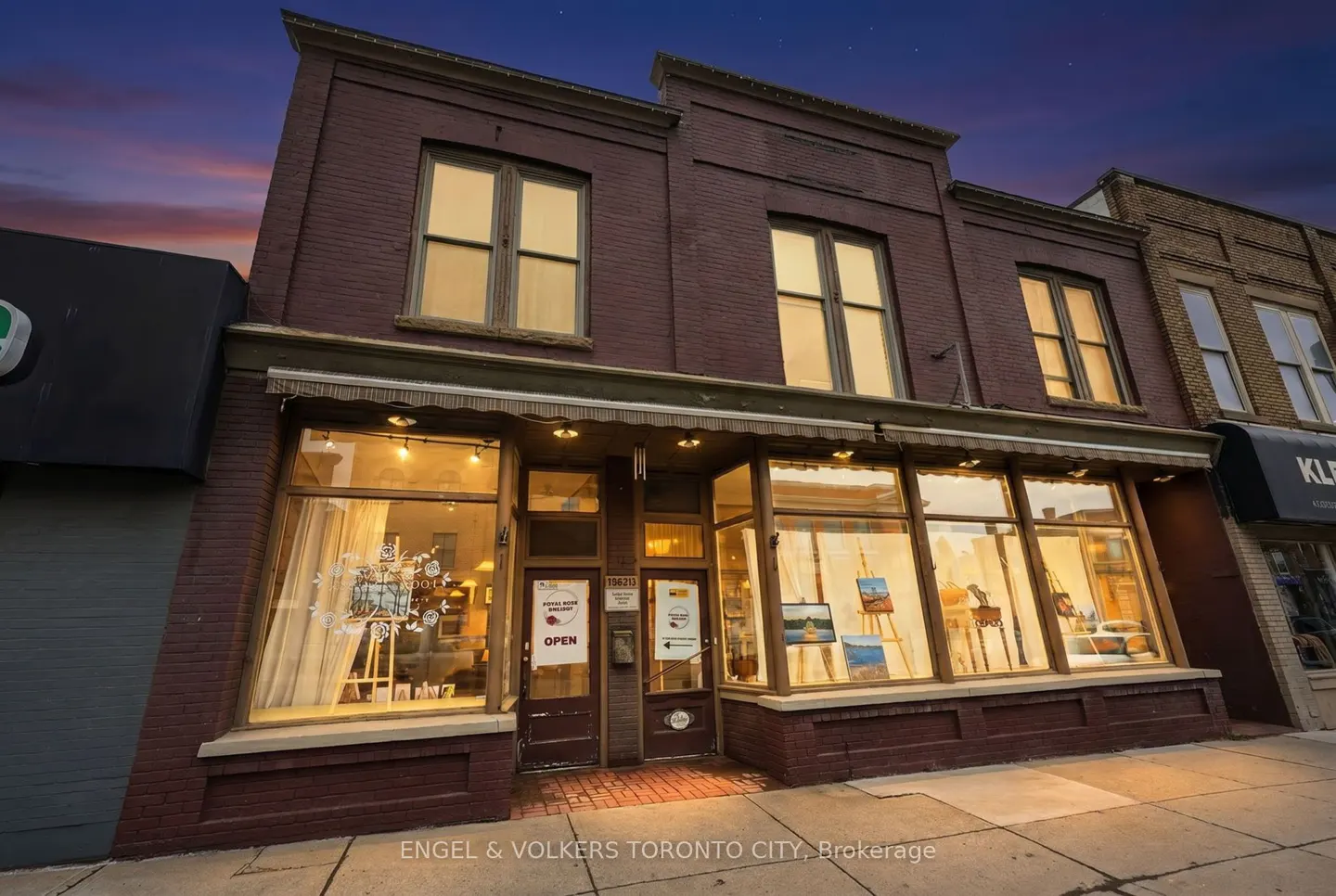 Two-story brick building with large storefront windows. An "open" sign is visible in the door. The sky is a twilight blue.