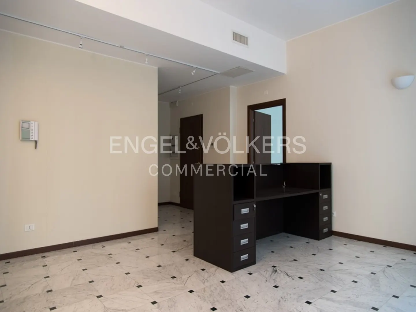 A commercial space with a dark brown desk, beige walls, and a white marble floor with black accents.