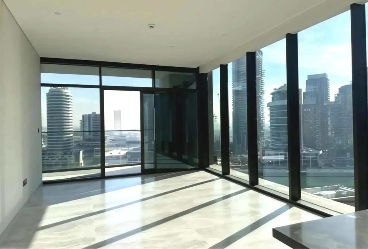 Bright, empty room with marble floors and floor-to-ceiling windows. A city skyline is visible through the windows.