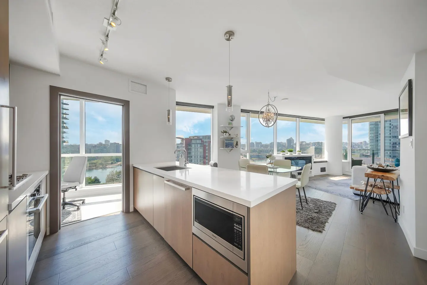 Bright, modern condo interior with a kitchen island, stainless steel appliances, and floor-to-ceiling windows with city views.