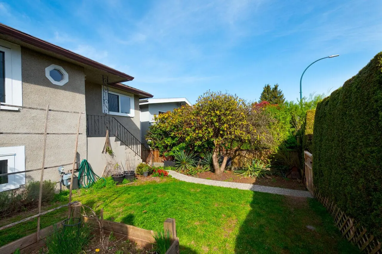 A house with a green lawn, a garden, and a tree with yellow leaves under a blue sky.