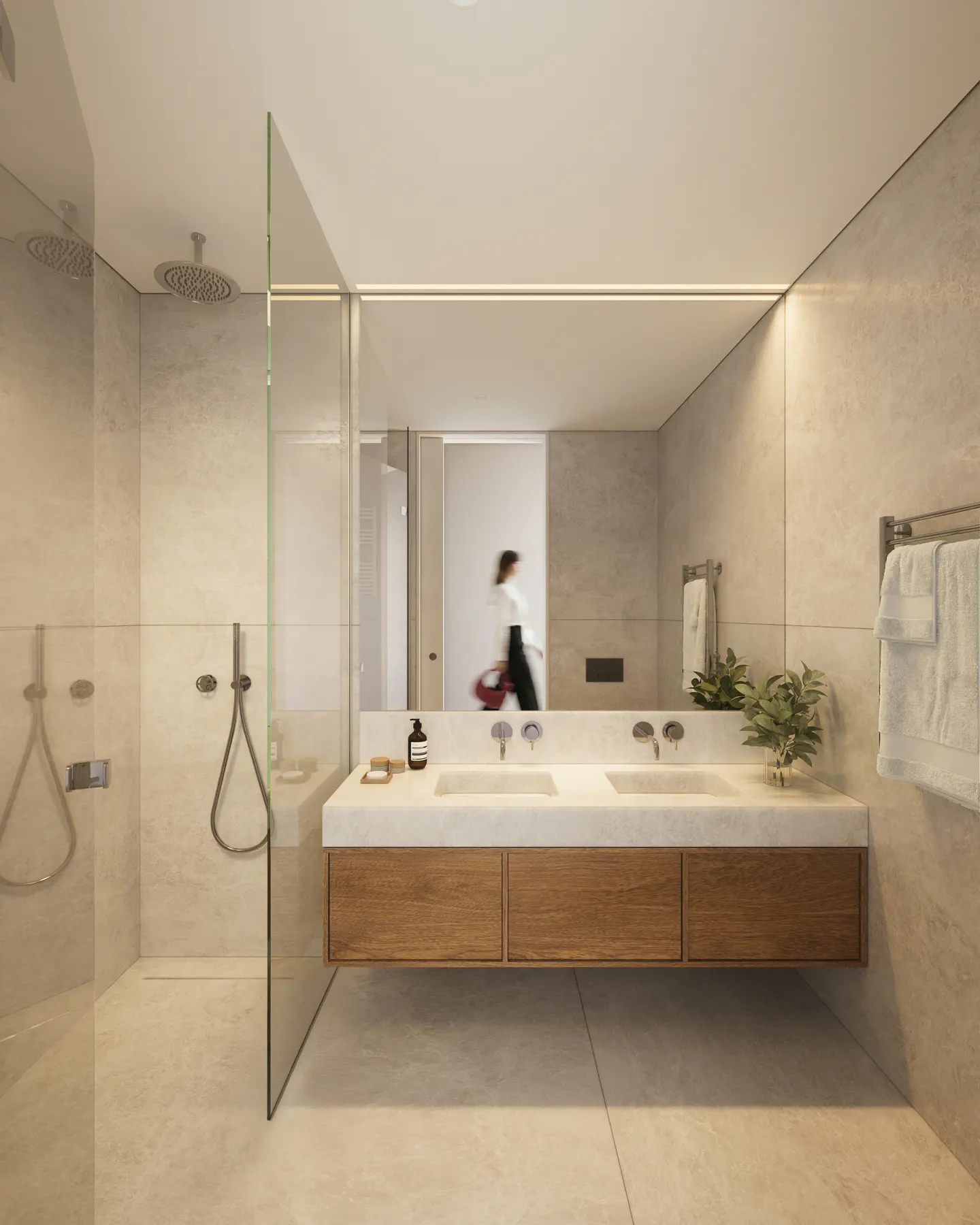 Modern bathroom with a glass shower, double sink vanity with wood cabinets, and a large mirror reflecting a person walking by.