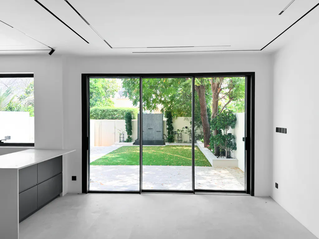 Bright, modern interior with white walls, gray cabinets, and black-framed sliding glass doors leading to a green lawn and garden.