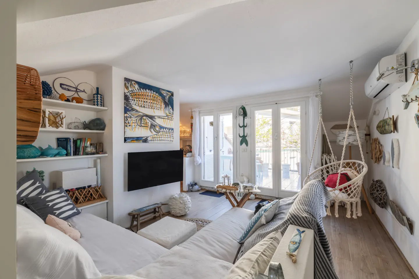 Bright living room with white sofa, fish-themed decor, and a hanging chair near glass doors to a balcony.