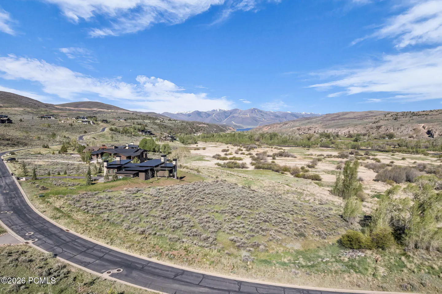 Scenic view of a modern home nestled in a valley, with mountains and a blue sky backdrop.