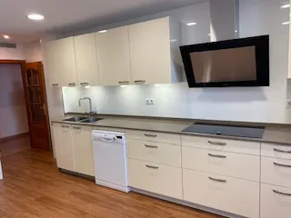 Modern kitchen with cream cabinets, wood floors, a white dishwasher, and a black range hood over a sleek countertop.