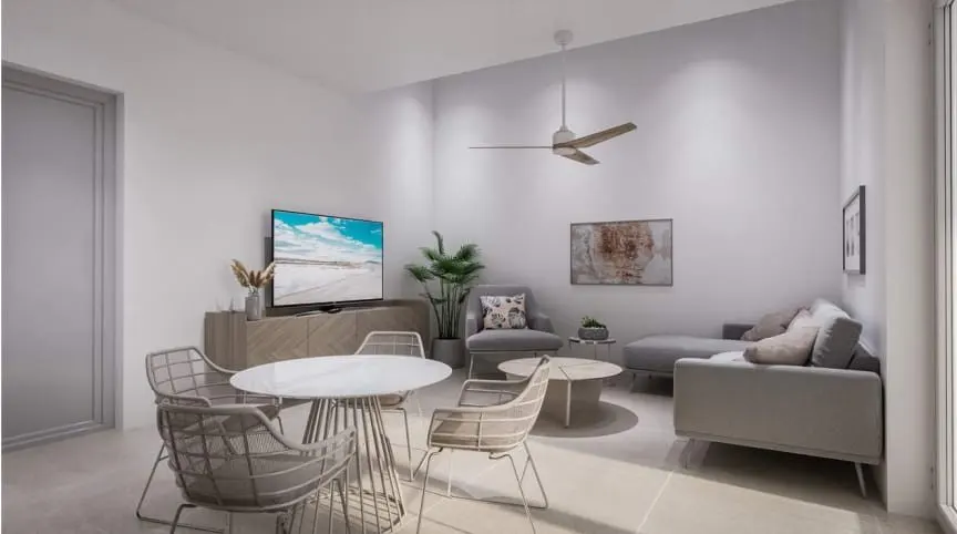 Bright living room with a white table and chairs, a gray sofa, and a TV showing a beach scene. A ceiling fan is overhead.