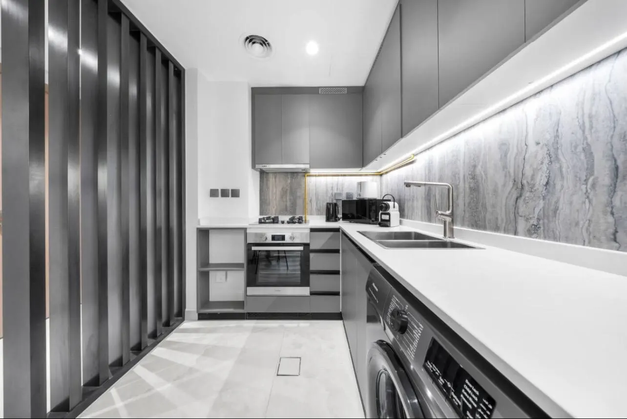A modern kitchen with gray cabinets, white countertops, and a marble backsplash. A black vertical slat wall is on the left.