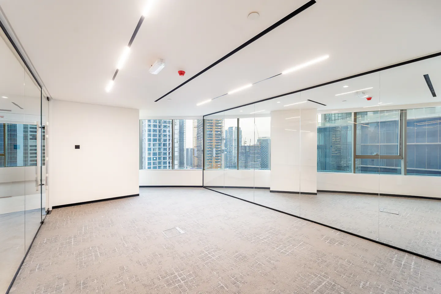Bright, empty office space with gray carpet, white walls, and floor-to-ceiling windows with city views.