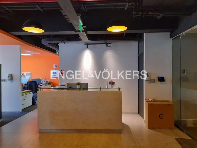 Engel & Völkers office reception area with a light wood desk, glass partition, and orange accent wall.