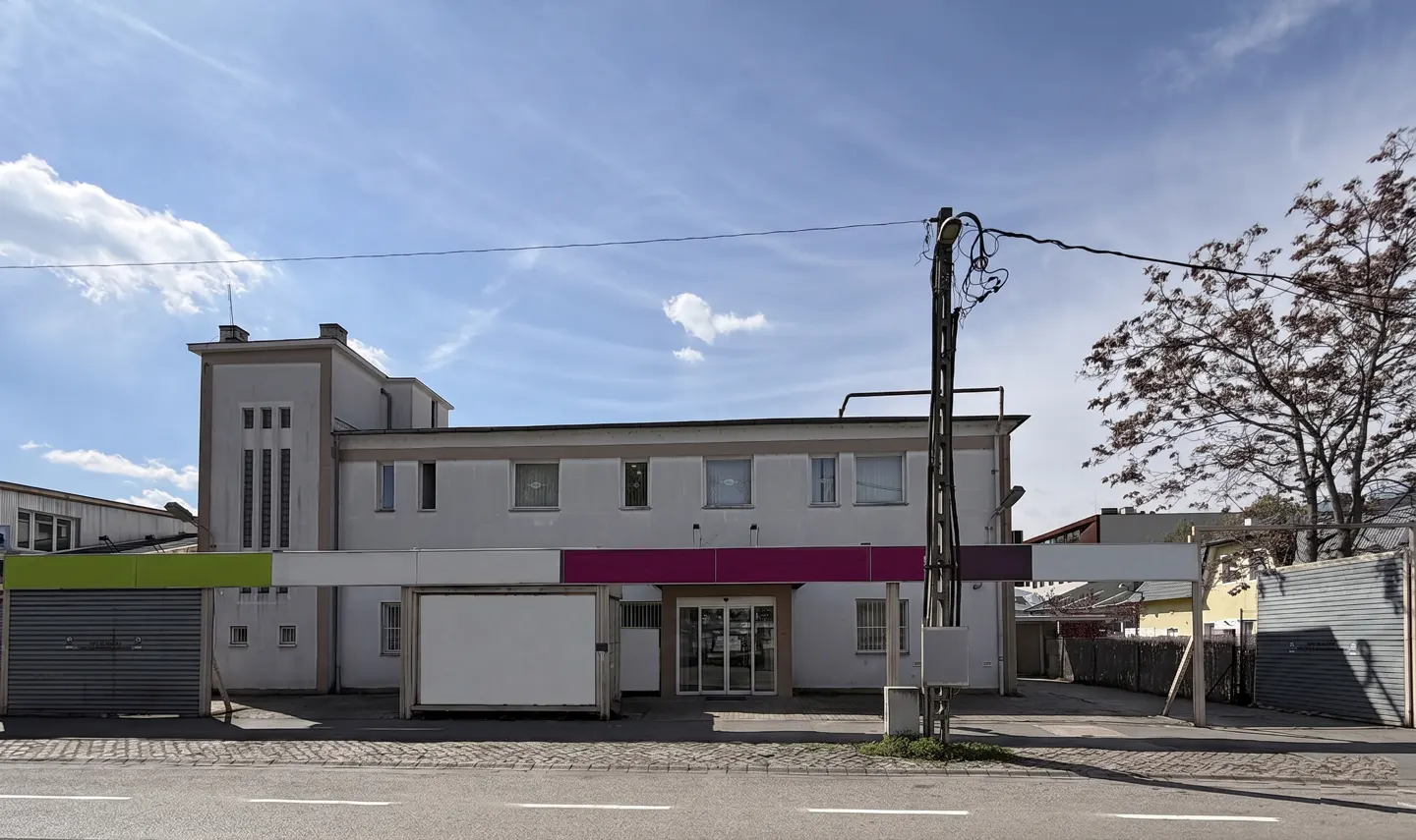 A two-story white building with a flat roof and a green and purple awning.