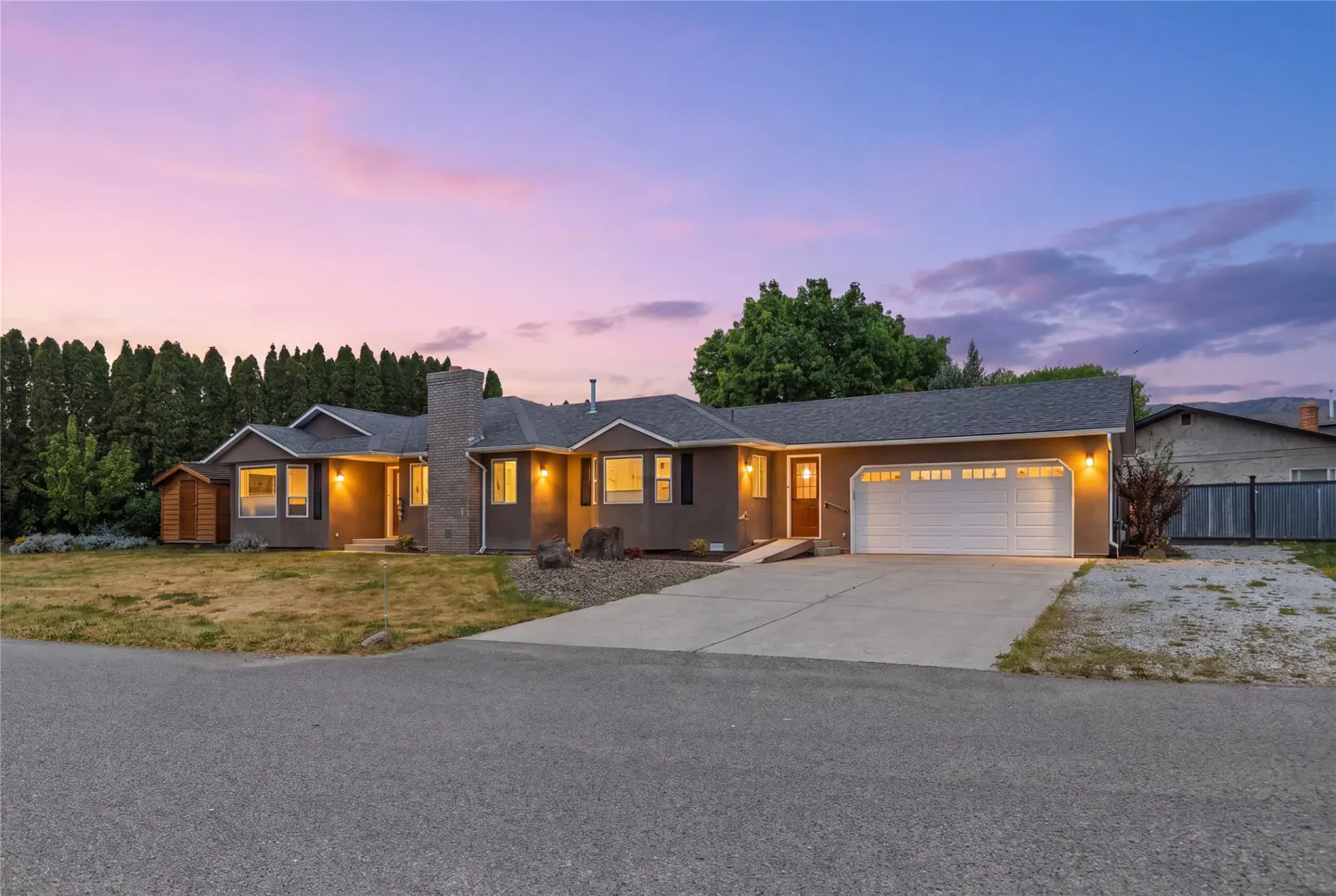 A single-story house with a gray roof, brown exterior, and white garage door at dusk.