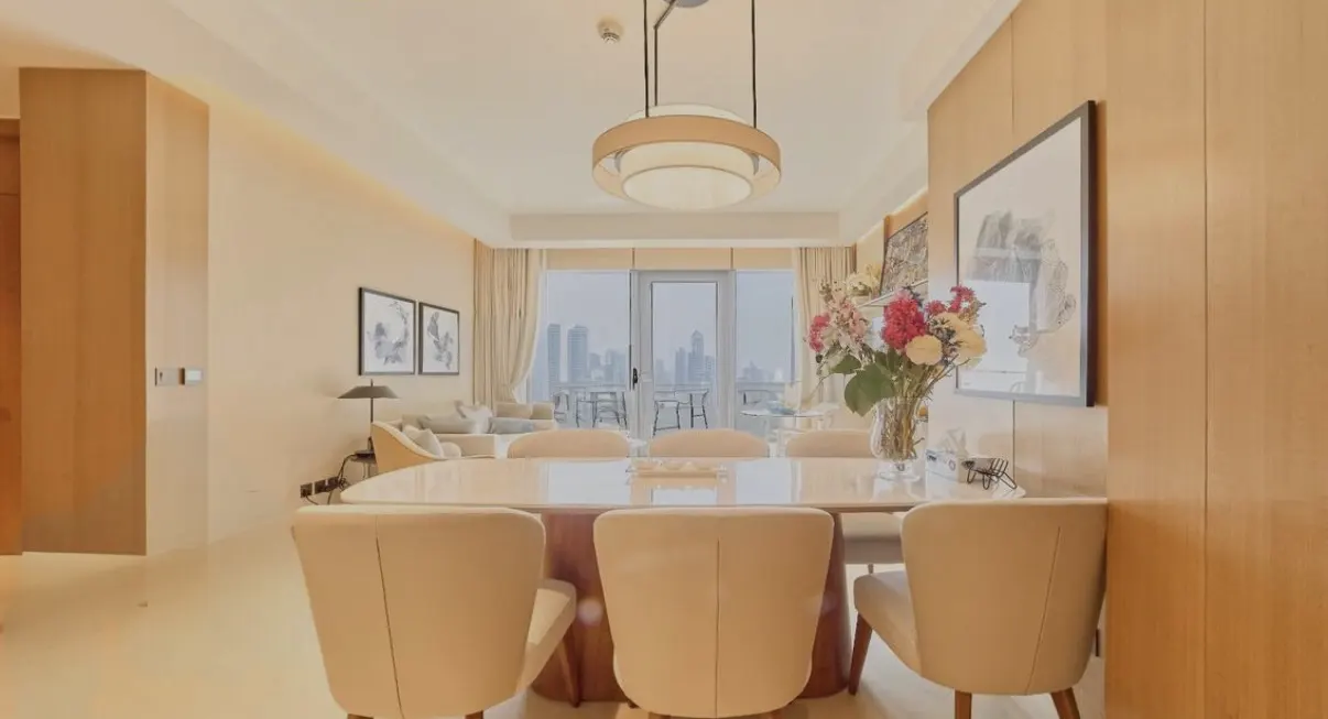 Modern dining room with a white table, cream chairs, a floral centerpiece, and a balcony view of a city skyline.