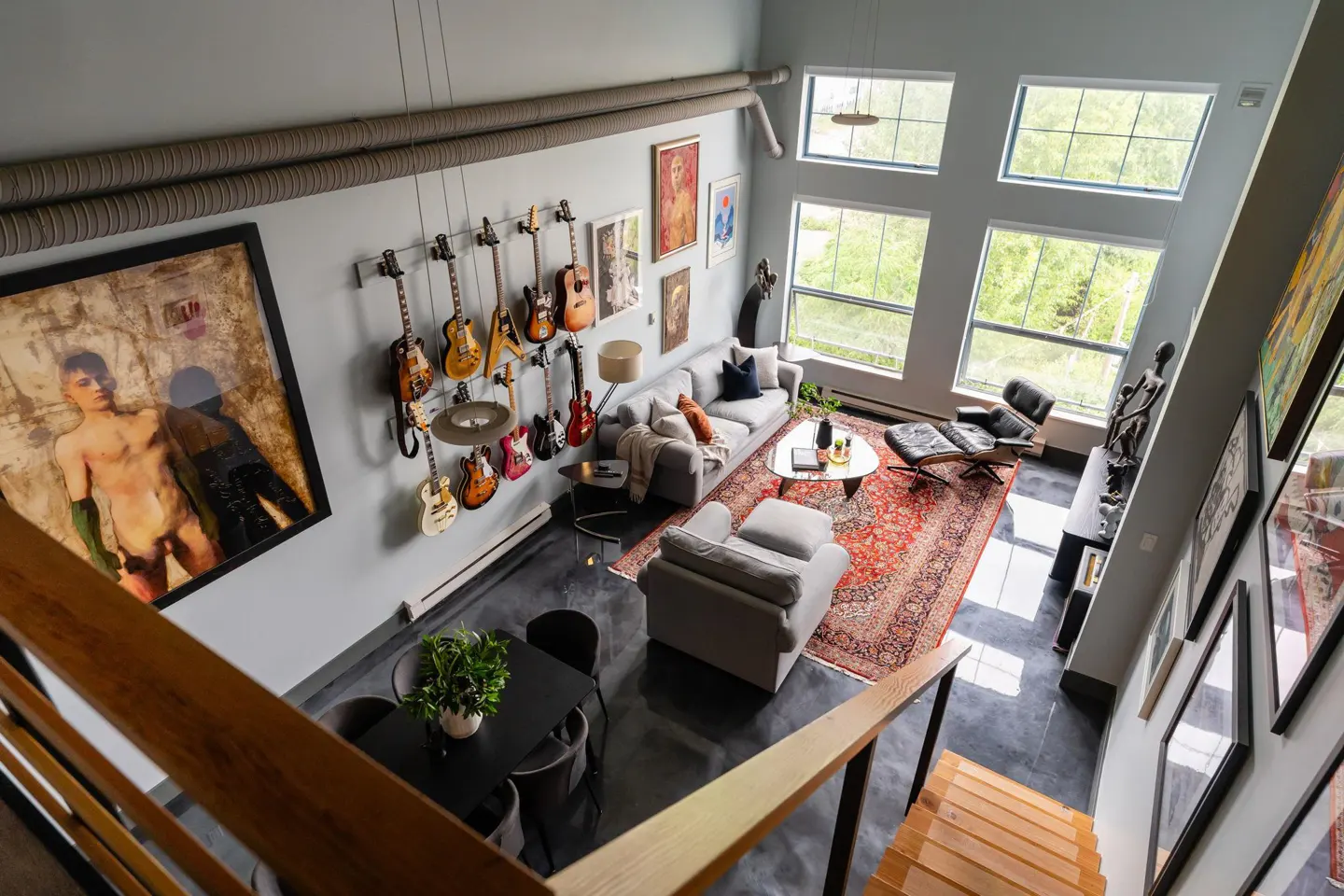High-angle view of a modern living room with gray walls, guitars on display, a gray sofa, and a red patterned rug. Large windows provide natural light.