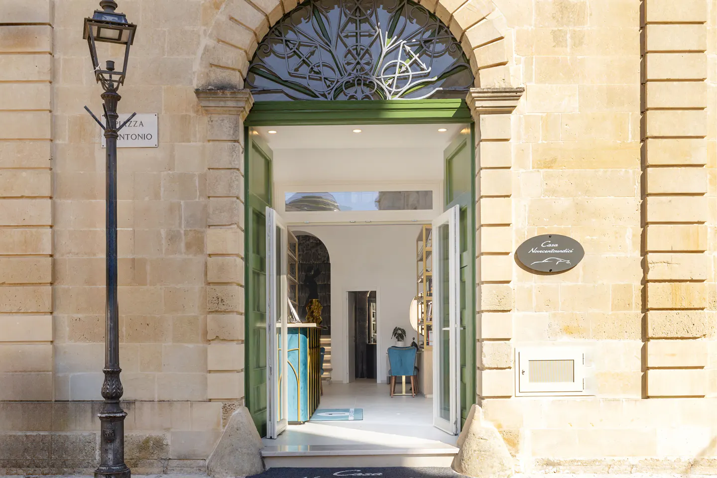 Exterior view of Casa Novecentoundici with open green doors and a black street lamp on the left.