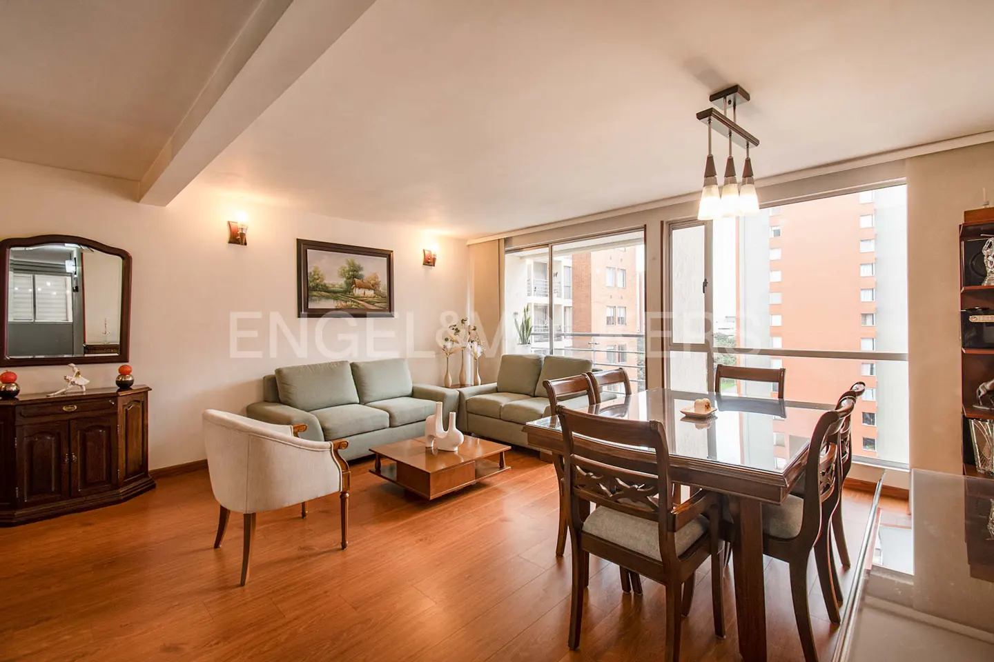Bright living and dining area with hardwood floors, light green sofas, a wooden dining table, and a large window with a city view.