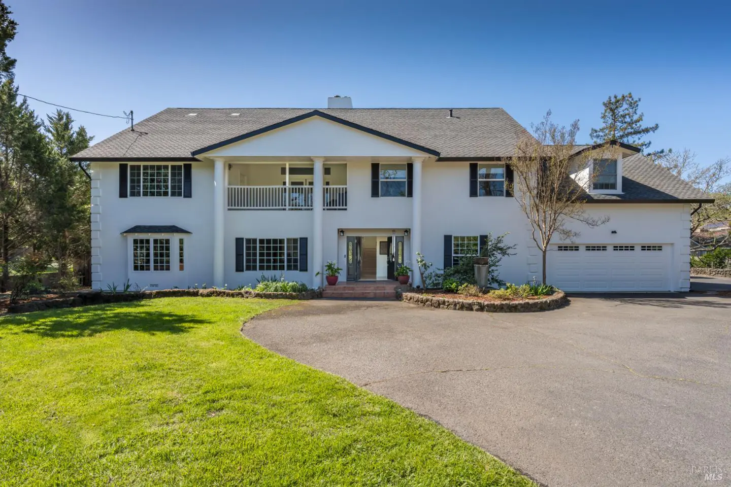 Two-story white house with black shutters, a gray roof, and a curved driveway. A green lawn is in the foreground.