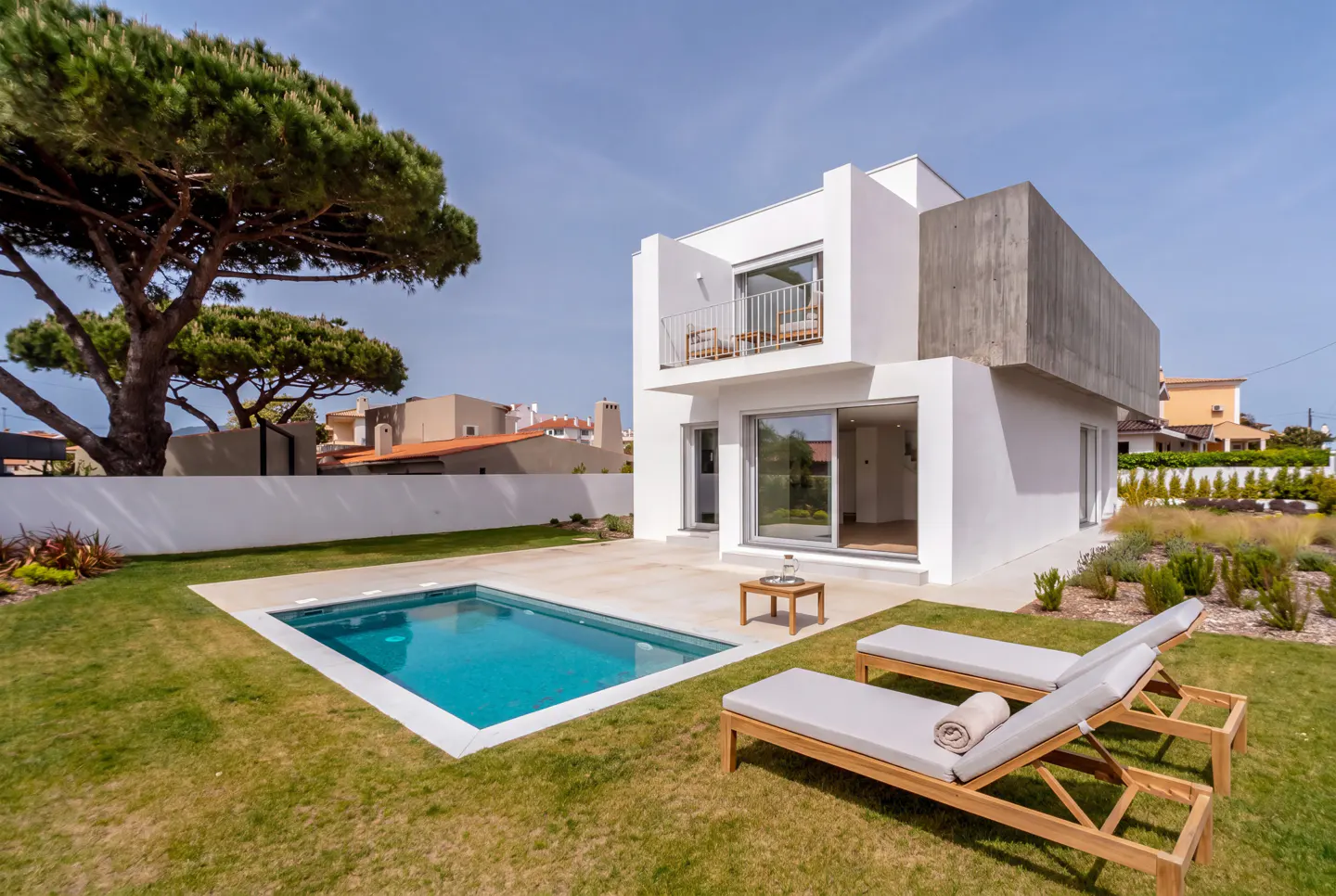 Modern white house with a pool and two lounge chairs on the green lawn.