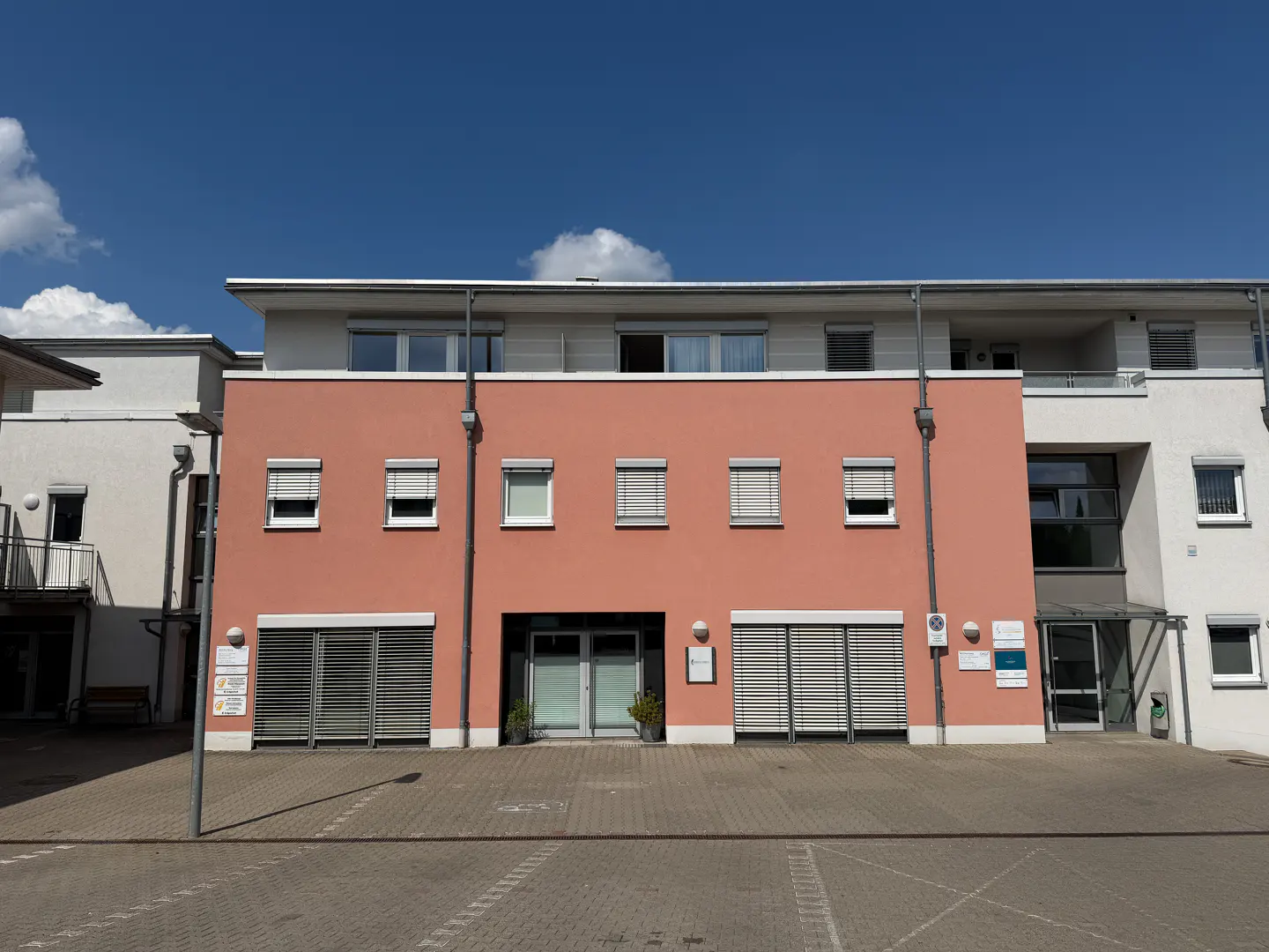Exterior view of a two-story building with a salmon-colored facade, gray shutters, and a blue sky background.